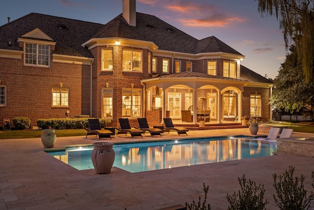 rear view of house featuring an outdoor pool, brick siding, a patio, and a chimney