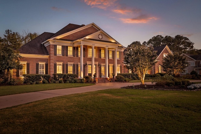 neoclassical / greek revival house featuring concrete driveway, a lawn, and brick siding