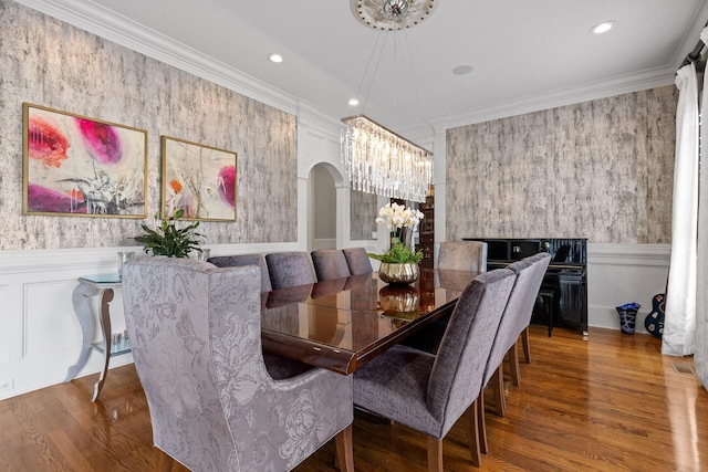 dining room with a chandelier, arched walkways, a wainscoted wall, and ornamental molding