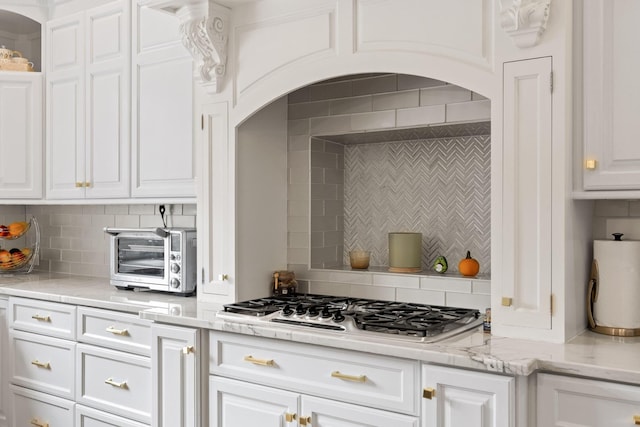 kitchen with a toaster, stainless steel gas cooktop, backsplash, white cabinetry, and light stone countertops