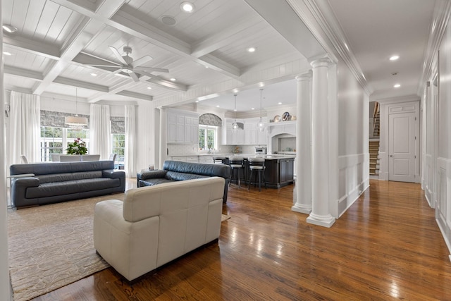 living area with beam ceiling, dark wood finished floors, ceiling fan, coffered ceiling, and ornate columns