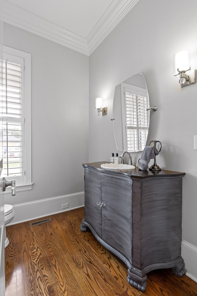 half bathroom featuring baseboards, visible vents, toilet, ornamental molding, and wood finished floors