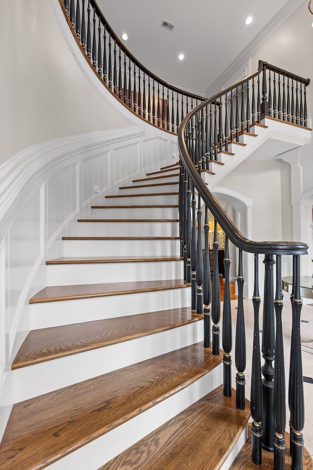 stairs with crown molding, recessed lighting, visible vents, and a decorative wall