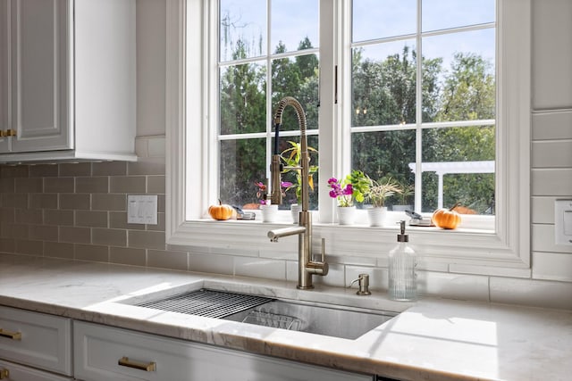 details featuring white cabinets, a sink, backsplash, and light stone countertops