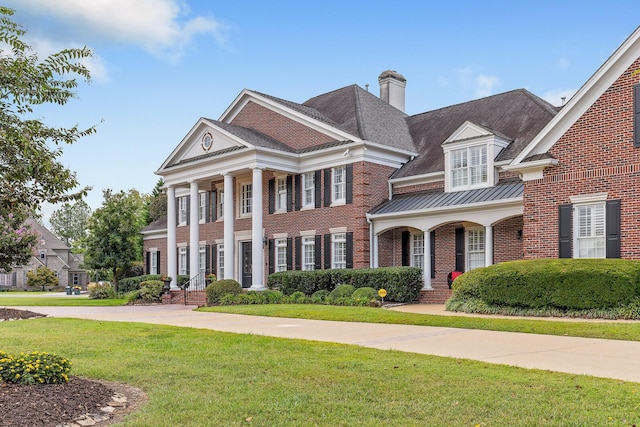 neoclassical / greek revival house with brick siding, a chimney, a standing seam roof, metal roof, and a front lawn