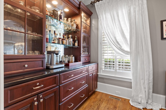 bar with a bar, baseboards, visible vents, and wood finished floors