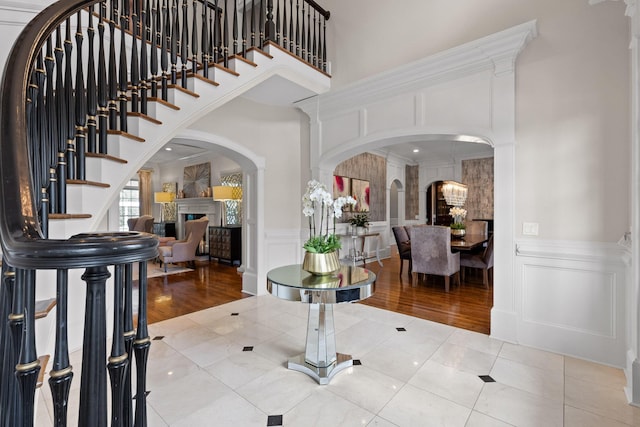 tiled foyer entrance with a towering ceiling, stairway, crown molding, a fireplace, and a decorative wall