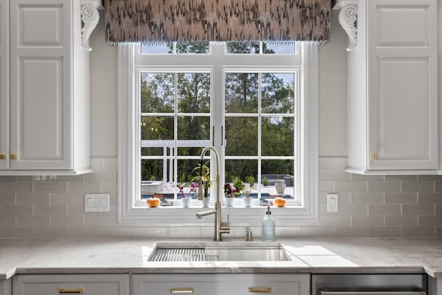 kitchen with backsplash, a sink, light stone countertops, and white cabinets