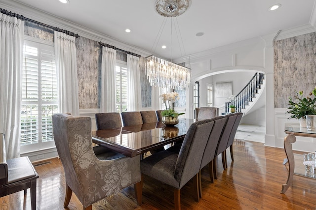 dining area with arched walkways, crown molding, visible vents, stairway, and wood finished floors