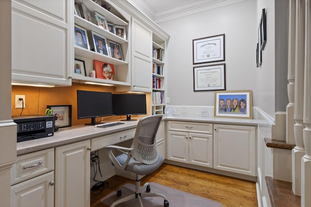 office space featuring light wood-style floors, ornamental molding, and built in desk