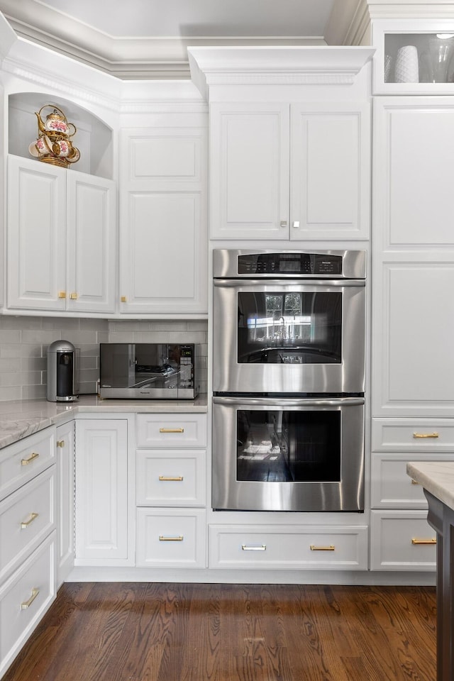 kitchen featuring light stone counters, dark wood finished floors, decorative backsplash, double oven, and white cabinets