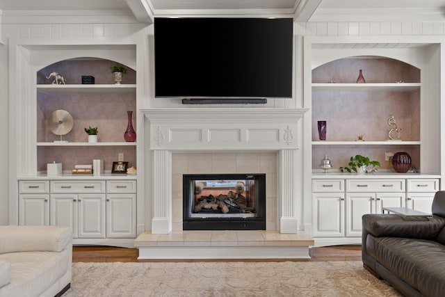 living room featuring built in shelves, a tile fireplace, light wood-style flooring, and crown molding