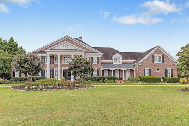 greek revival house with a front yard, a chimney, and brick siding