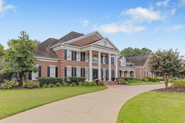 greek revival inspired property with concrete driveway, brick siding, and a front yard