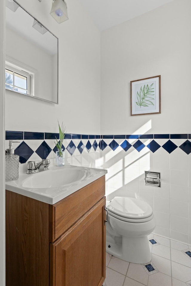 bathroom with tile walls, toilet, wainscoting, vanity, and tile patterned flooring