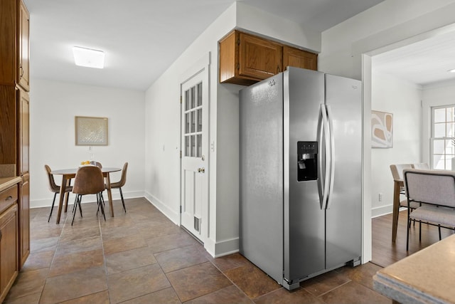 kitchen featuring brown cabinets, baseboards, stainless steel refrigerator with ice dispenser, and light countertops