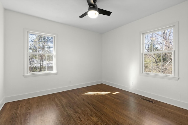 spare room featuring dark wood-type flooring, a wealth of natural light, visible vents, and baseboards