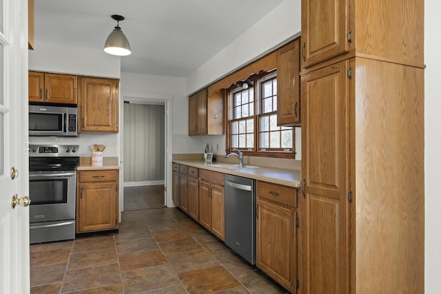 kitchen featuring appliances with stainless steel finishes, brown cabinets, decorative light fixtures, light countertops, and a sink