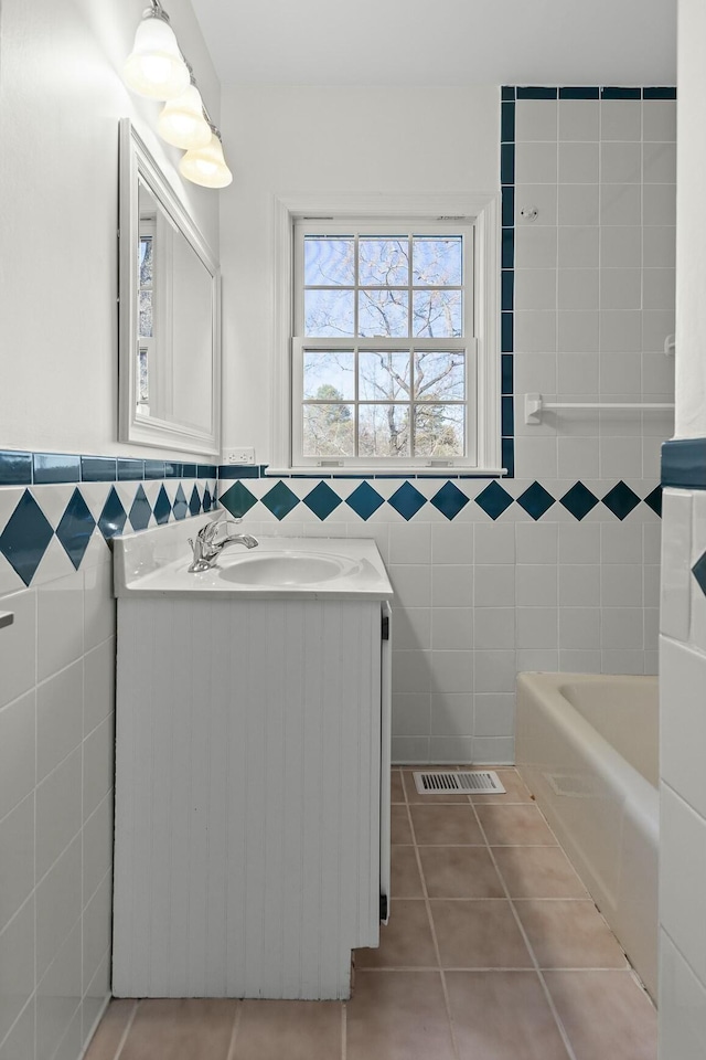 bathroom featuring a tub to relax in, tile walls, wainscoting, vanity, and tile patterned flooring