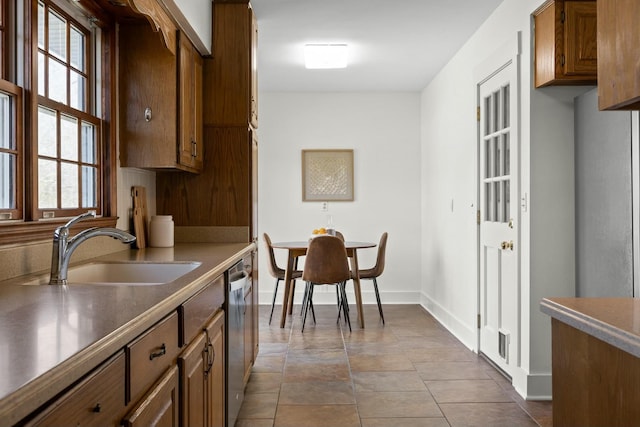 kitchen with dishwasher, brown cabinets, a sink, and baseboards