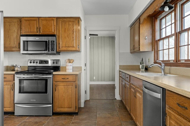 kitchen with stainless steel appliances, brown cabinetry, a sink, and tasteful backsplash