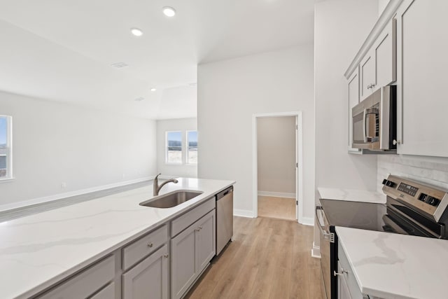 kitchen with light stone counters, light wood-style flooring, recessed lighting, a sink, and appliances with stainless steel finishes