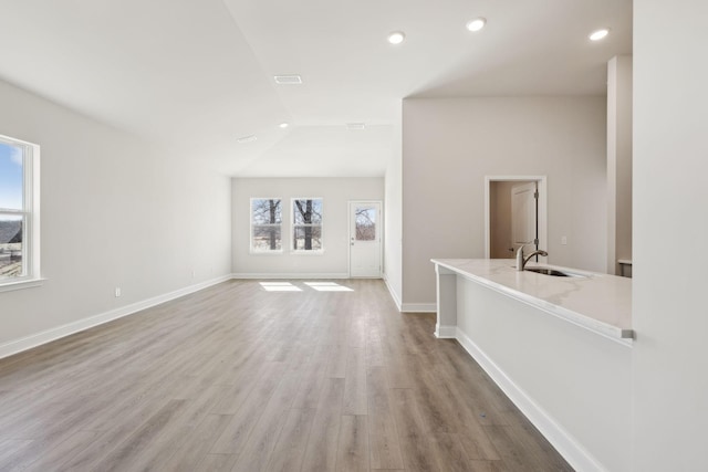 unfurnished living room with light wood finished floors, baseboards, visible vents, lofted ceiling, and a sink