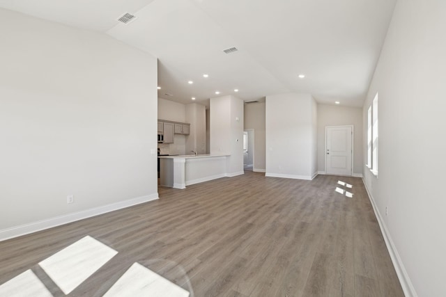 unfurnished living room featuring light wood-type flooring, visible vents, vaulted ceiling, and baseboards