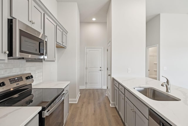 kitchen with tasteful backsplash, stainless steel appliances, gray cabinetry, light wood-type flooring, and a sink