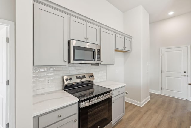 kitchen with stainless steel appliances, light stone counters, backsplash, and gray cabinets