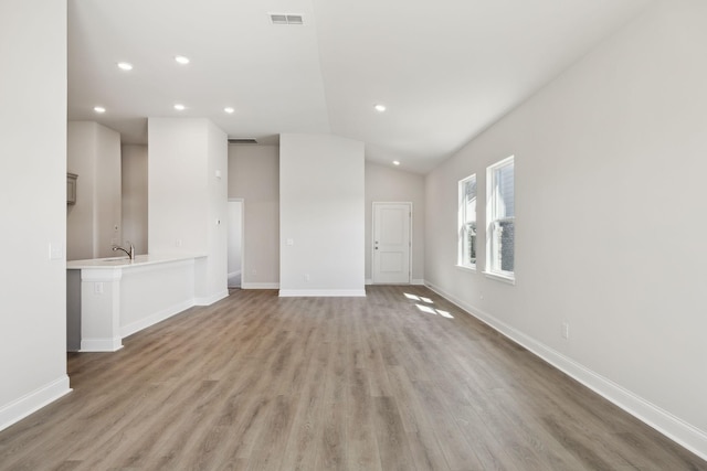 unfurnished living room featuring light wood finished floors, lofted ceiling, recessed lighting, visible vents, and baseboards