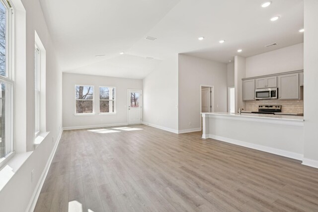 unfurnished living room featuring lofted ceiling, recessed lighting, light wood-style flooring, and baseboards