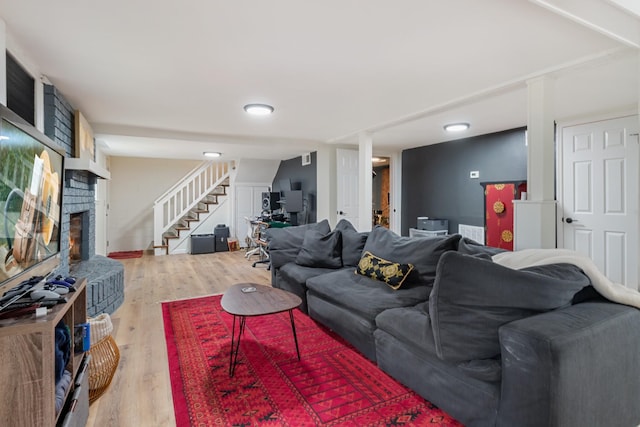 living room with stairs, a fireplace with raised hearth, and wood finished floors