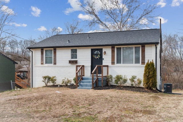 view of front of house with a shingled roof, cooling unit, brick siding, and a front lawn