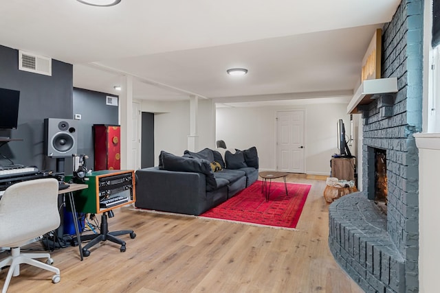 living area featuring a brick fireplace, visible vents, baseboards, and wood finished floors