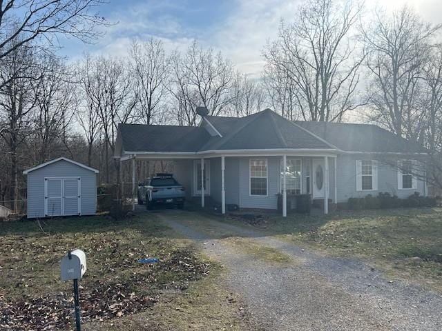 ranch-style house featuring an attached carport, a storage shed, an outdoor structure, driveway, and a chimney