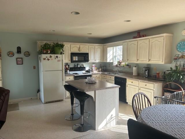 kitchen featuring a center island, baseboards, a sink, black appliances, and a kitchen bar