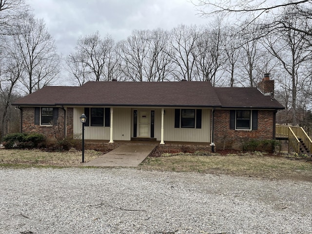 single story home with gravel driveway, a chimney, a porch, and brick siding