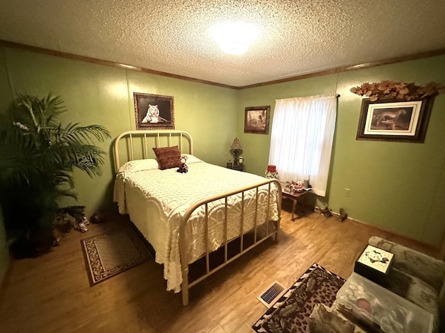 bedroom with crown molding, a textured ceiling, visible vents, and wood finished floors