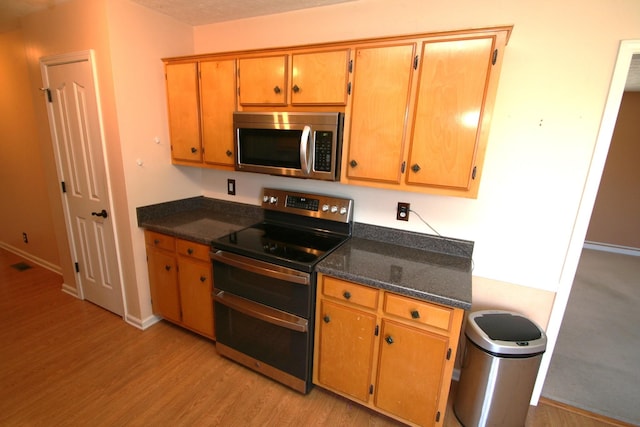 kitchen with baseboards, visible vents, appliances with stainless steel finishes, dark stone countertops, and light wood-type flooring