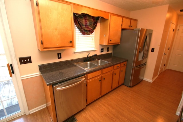 kitchen with baseboards, dark countertops, stainless steel appliances, light wood-type flooring, and a sink