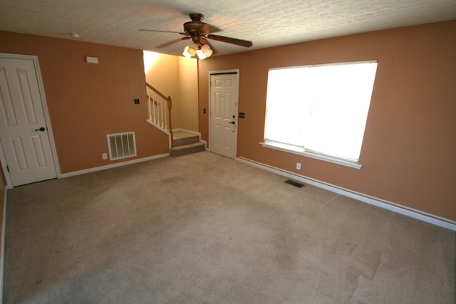 empty room featuring stairs, a ceiling fan, visible vents, and light colored carpet