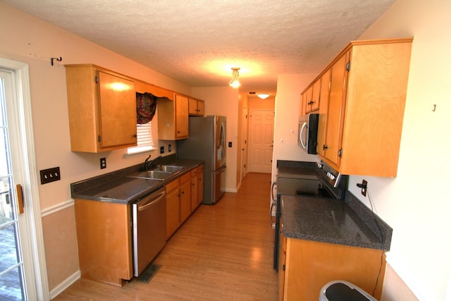 kitchen featuring dark countertops, light wood-type flooring, stainless steel appliances, and a sink