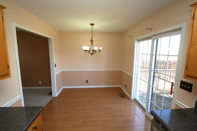 unfurnished dining area featuring light wood finished floors, baseboards, visible vents, and a notable chandelier