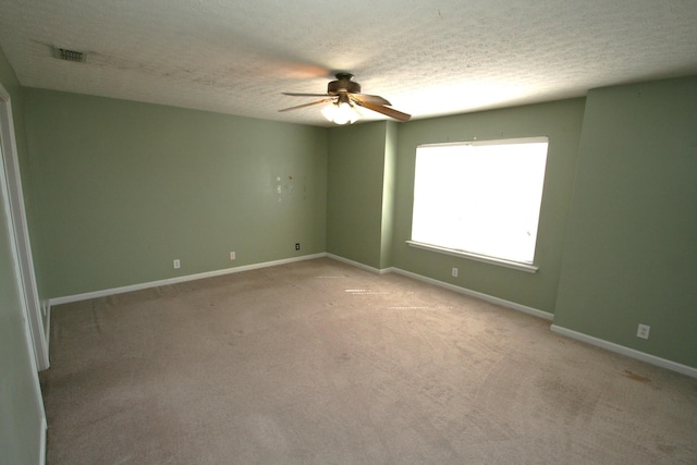 empty room featuring light colored carpet, visible vents, a ceiling fan, a textured ceiling, and baseboards