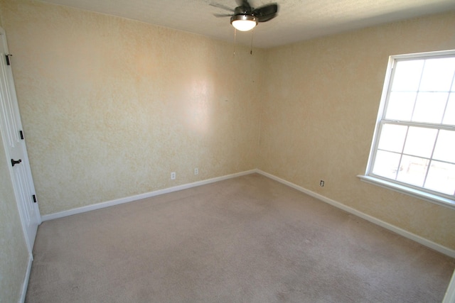 carpeted spare room featuring ceiling fan and baseboards