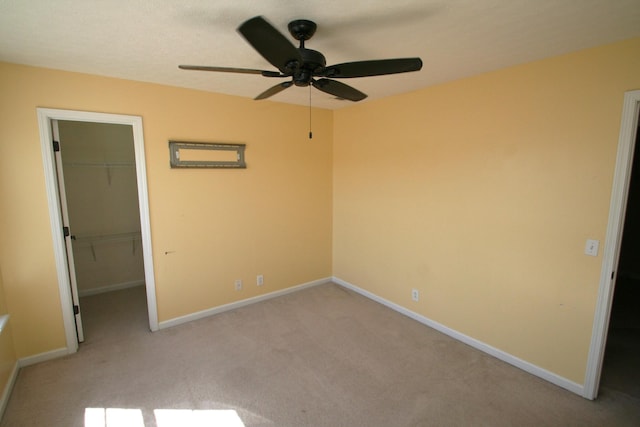 unfurnished bedroom featuring baseboards, a walk in closet, a closet, and light colored carpet