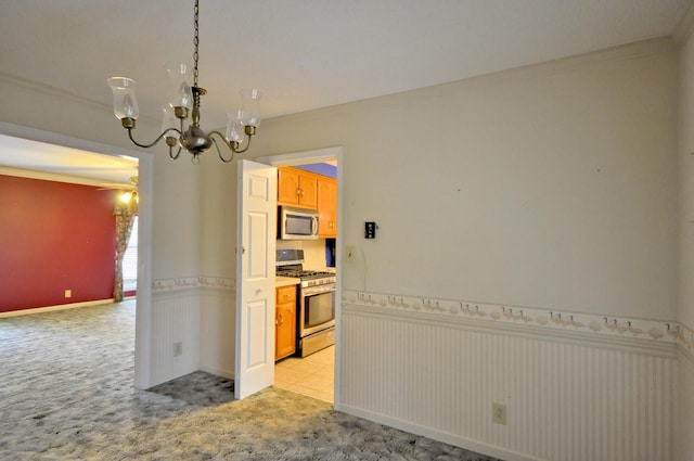 spare room with a wainscoted wall, crown molding, a notable chandelier, and light colored carpet