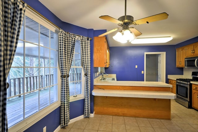 kitchen featuring light tile patterned floors, stainless steel appliances, a peninsula, light countertops, and brown cabinets