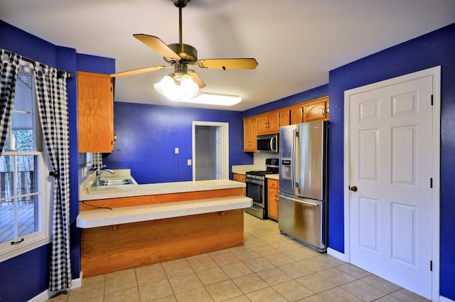 kitchen with light tile patterned floors, light countertops, appliances with stainless steel finishes, a sink, and a peninsula